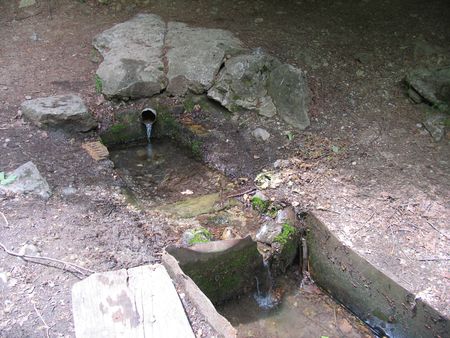 вода родника из каменного бассейна перетекает в железное корыто